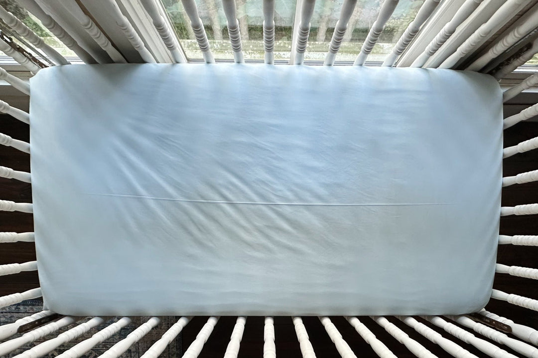 Heirloom Blue fitted crib sheet seen from above on a crib mattress, smooth across the surface with fitted corners - High Cotton Textile
