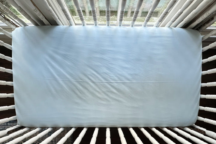 Heirloom Blue fitted crib sheet seen from above on a crib mattress, smooth across the surface with fitted corners - High Cotton Textile
