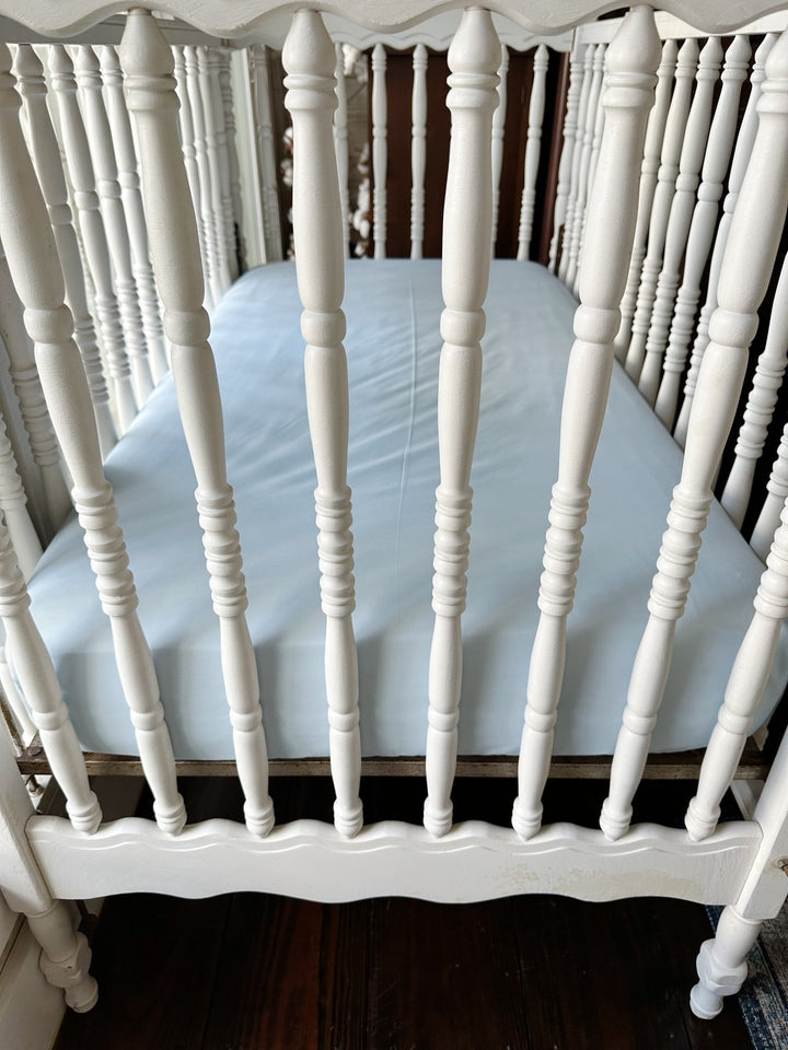 Heirloom Blue fitted crib sheet seen through the turned spindles of a white crib - High Cotton Textile