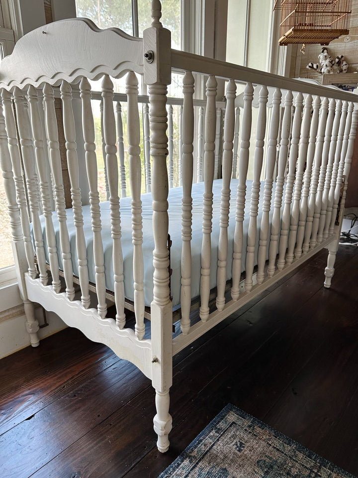 Angled view of a white spindle crib with the Heirloom Blue fitted crib sheet on the mattress - High Cotton Textile