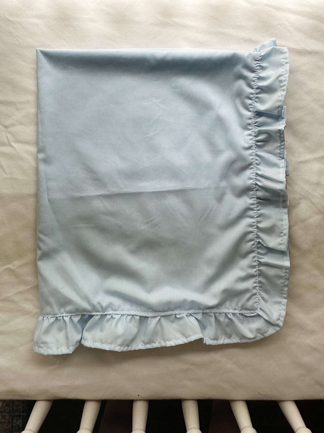Folded light blue ruffled baby blanket for a baby boy nursery resting on a crib mattress - High Cotton Textile