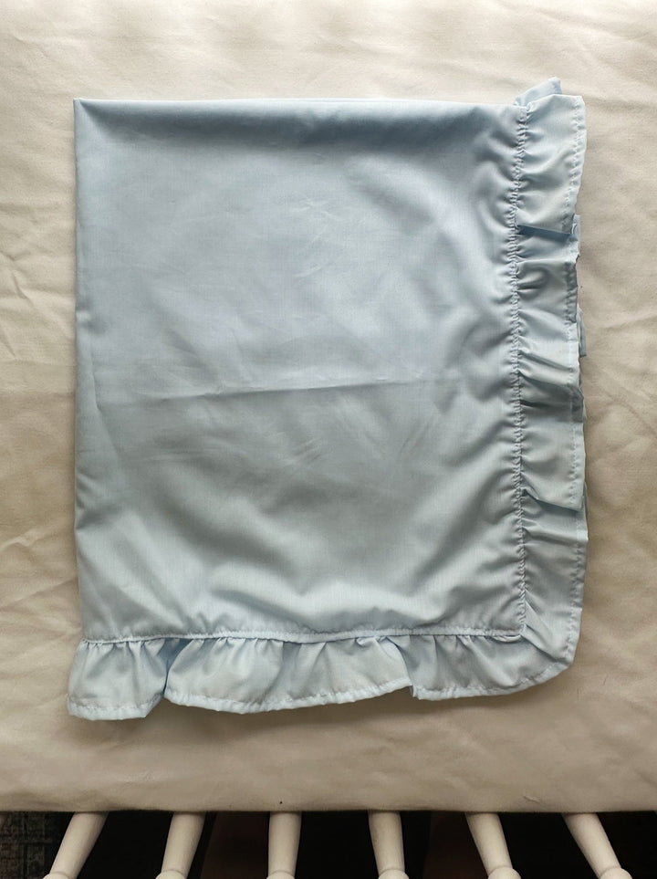 Folded light blue ruffled baby blanket for a baby boy nursery resting on a crib mattress - High Cotton Textile
