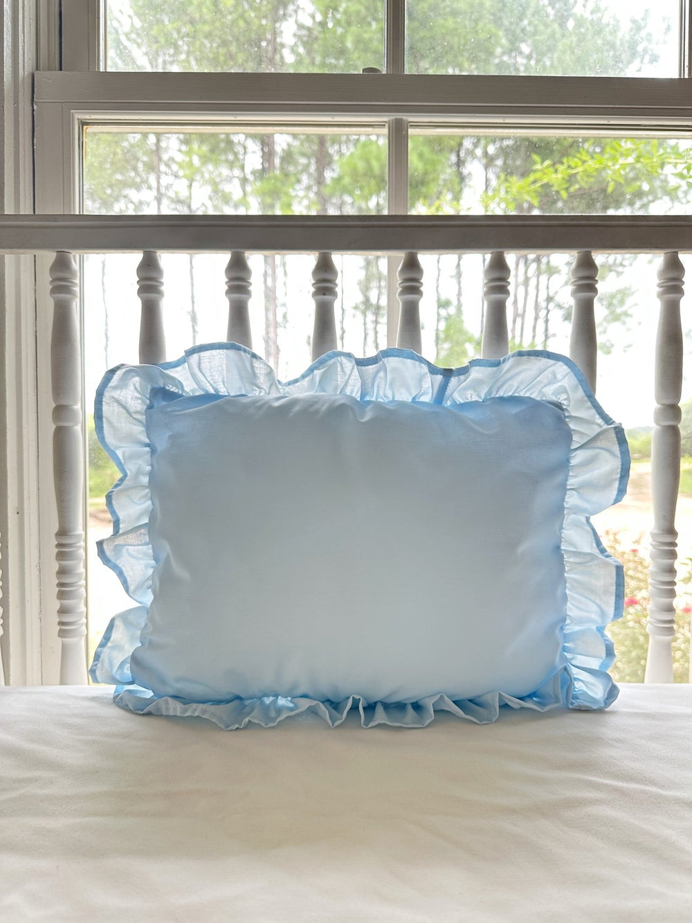 Light blue ruffled nursery pillow styled on a white spindle crib in a sunlit farmhouse nursery - High Cotton Textile