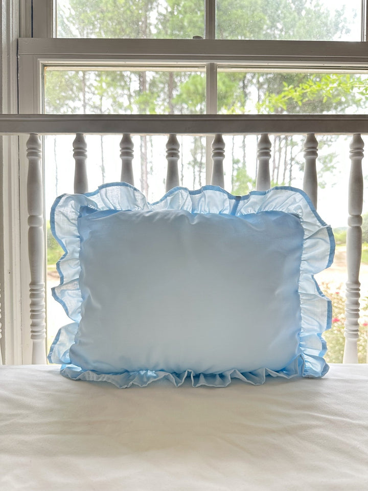 Light blue ruffled nursery pillow styled on a white spindle crib in a sunlit farmhouse nursery - High Cotton Textile