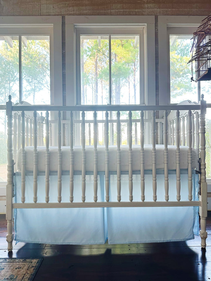 Straight-on view of the heirloom blue tailored crib skirt in soft morning light, the hem falling just to the dark pine floor - High Cotton Textile