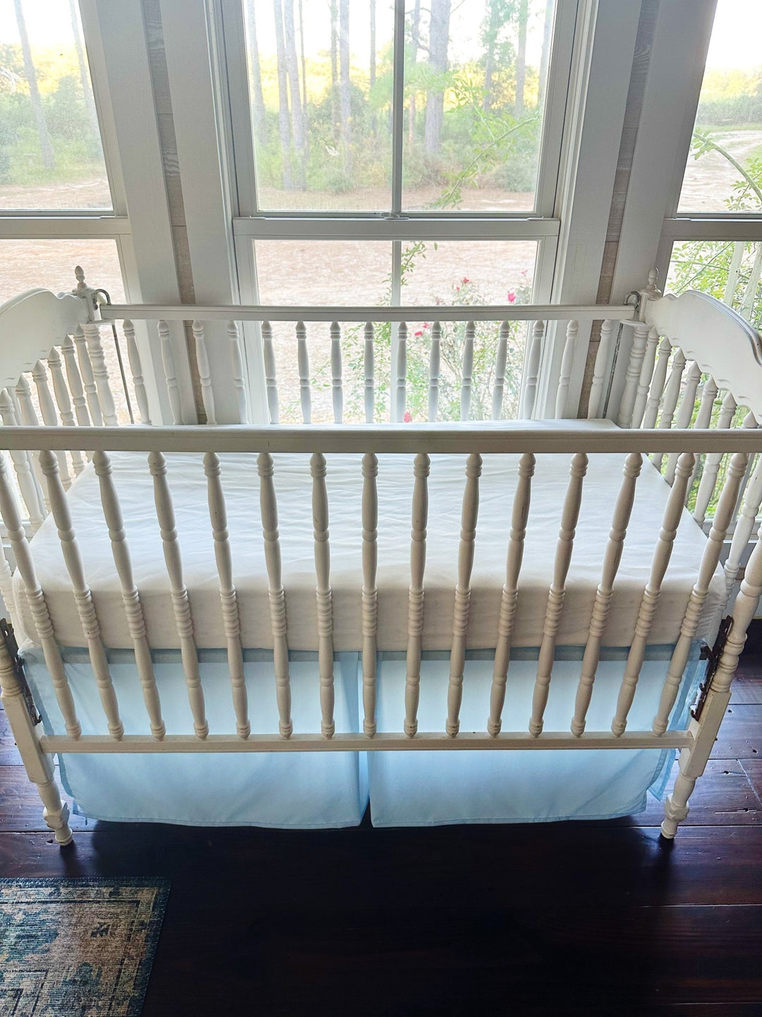 Heirloom blue tailored crib skirt on a white spindle crib, seen from the long side with the pleated center panel at the middle - High Cotton Textile