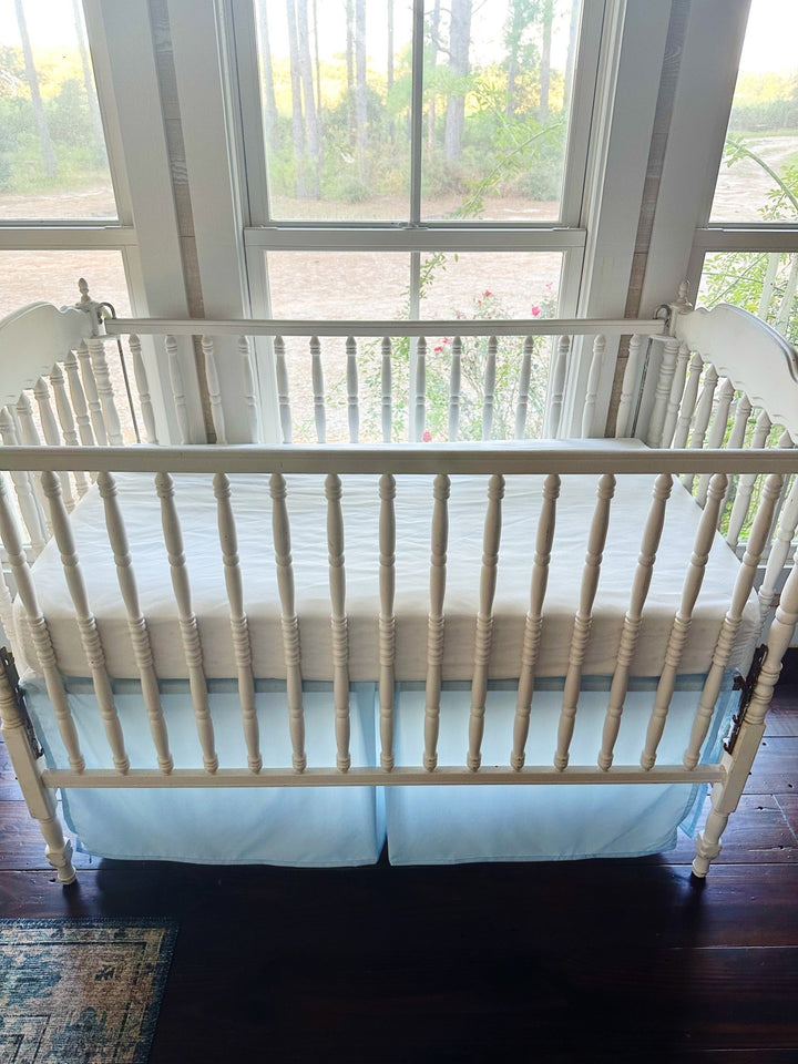 Heirloom blue tailored crib skirt on a white spindle crib, seen from the long side with the pleated center panel at the middle - High Cotton Textile