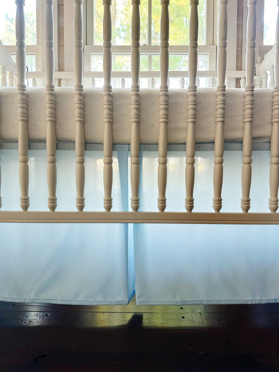 Close up through the crib spindles of the heirloom blue skirt's pleated center panel, backlit by a sunny window - High Cotton Textile
