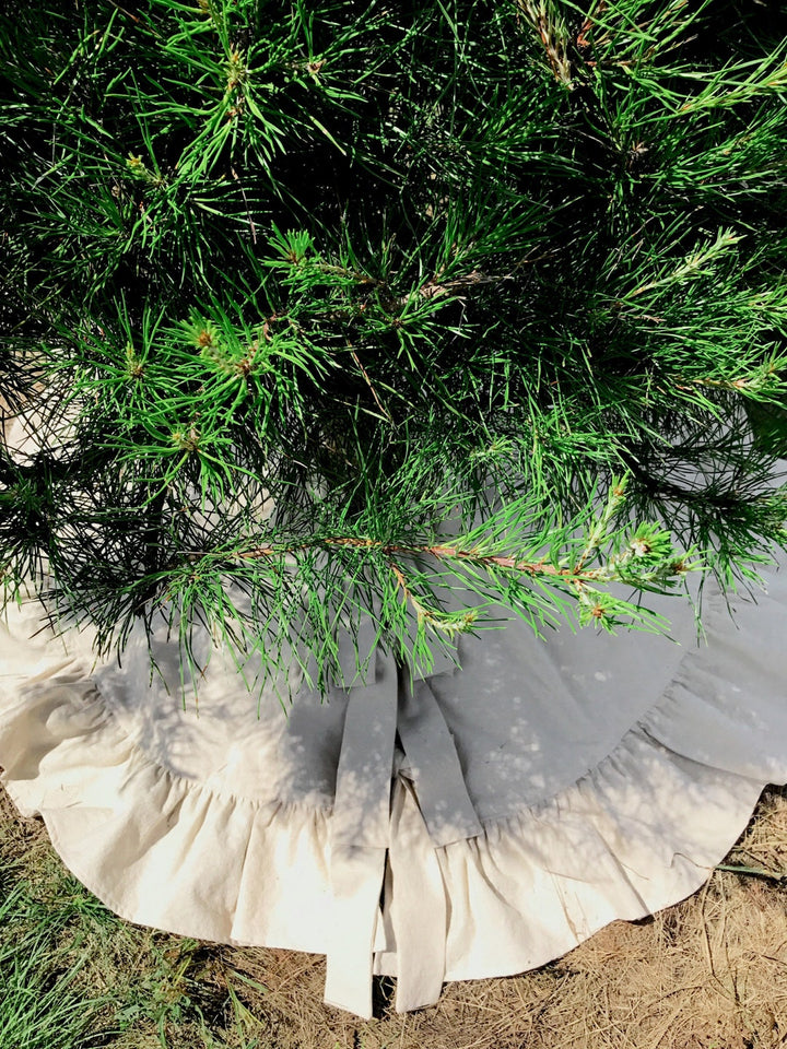 Pine branches over the natural ruffled tree skirt, sash ties visible at the front in afternoon sun