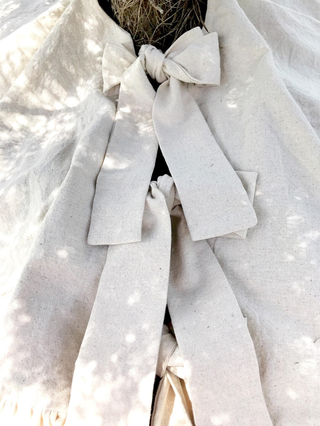 Natural osnaburg tie knotted into a bow at the trunk, long tails resting on the skirt in dappled light