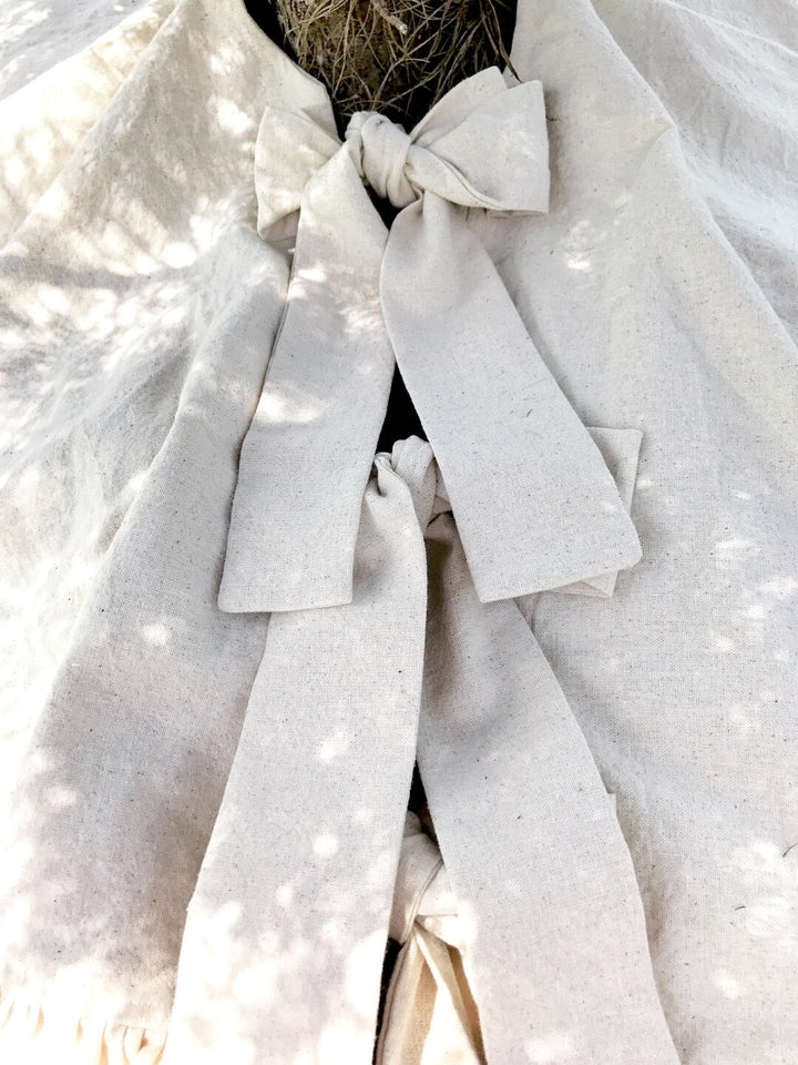 Natural osnaburg tie knotted into a bow at the trunk, long tails resting on the skirt in dappled light