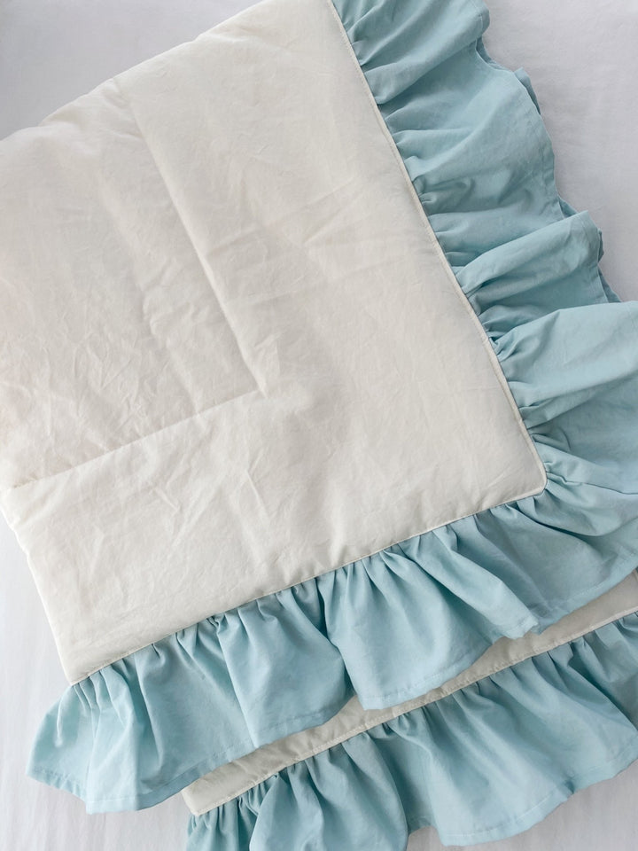 Flat detail of the ivory quilt panel and its double gathered mist blue cotton ruffle