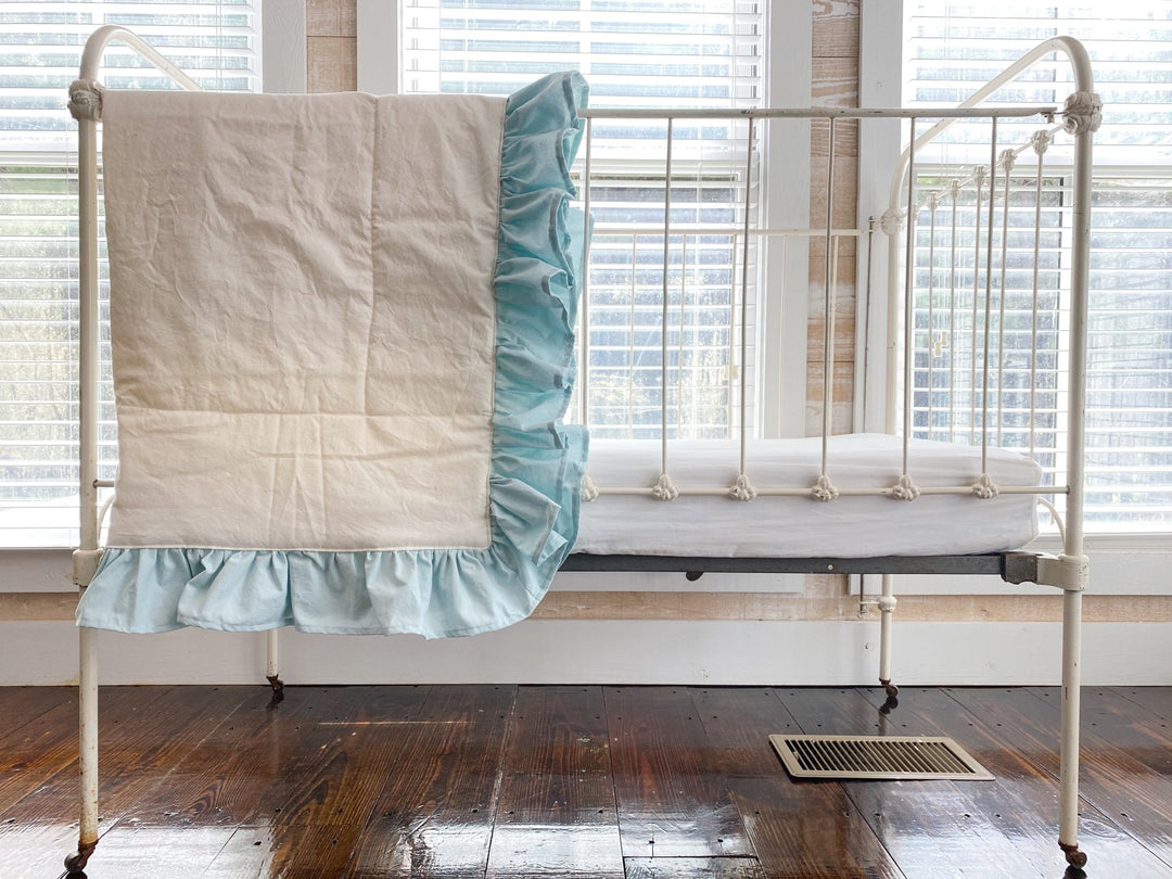 Ivory and mist ruffled baby quilt hung over the end of an antique white iron crib