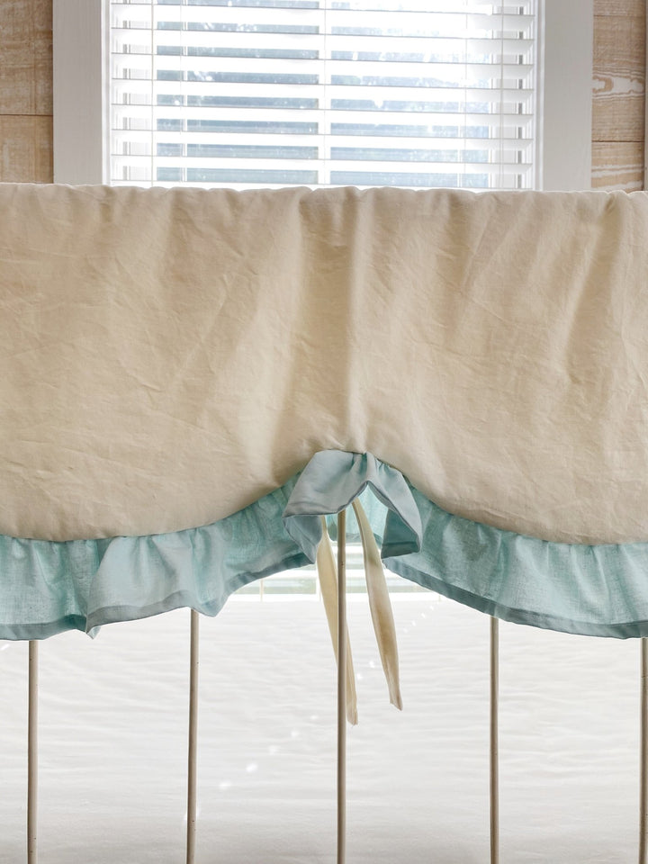 Detail of the center scallop and mist blue ruffle with ivory ties hanging from the crib rail cover