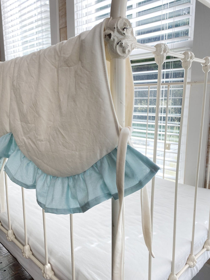 Close-up of a scalloped curve edged in mist blue ruffle with ivory cotton ties on a crib rail
