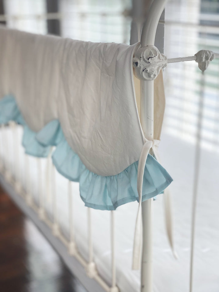 Side view of the ivory crib rail cover draping over an iron crib rail with a mist ruffle
