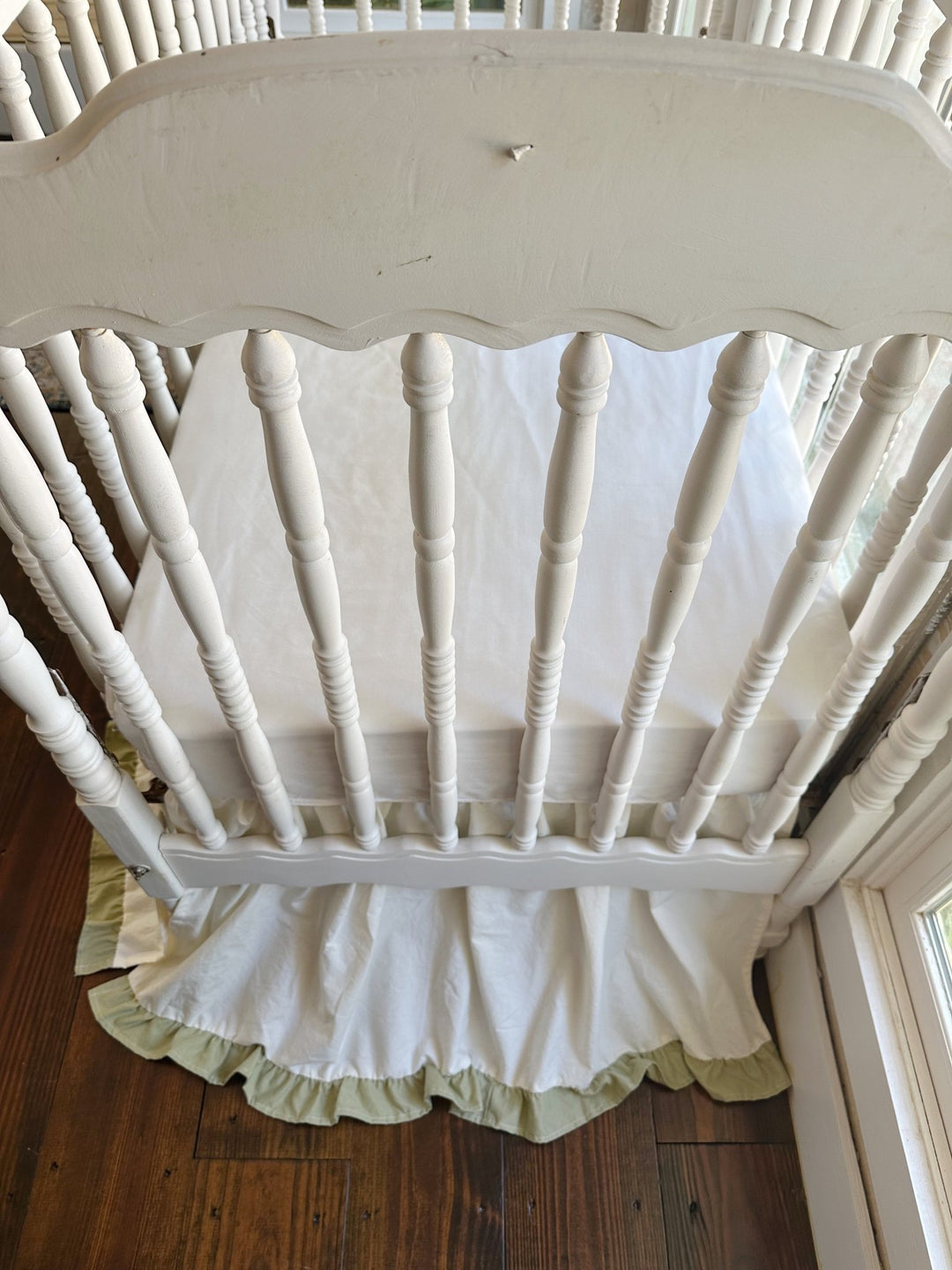 Ivory ruffled crib skirt with sage green hem seen from inside the crib, showing full floor length coverage