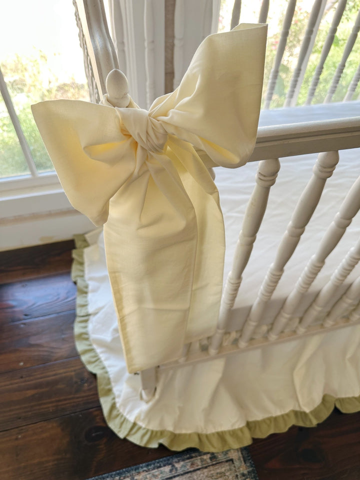 Close up of a large ivory crib bow sash tied in a full knot on a turned crib post
