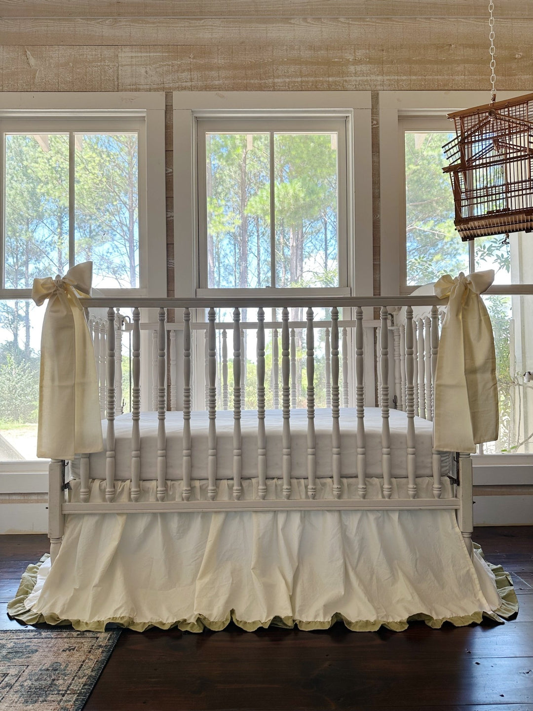Front view of a neutral crib bedding set with ivory ruffled crib skirt, sage green hem and two ivory bow sashes