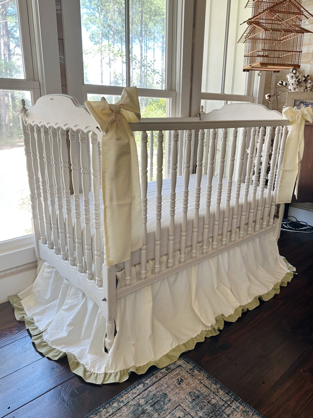 Ivory and sage ruffled crib skirt with two large ivory crib bows tied to an antique white spindle crib - High Cotton Textile