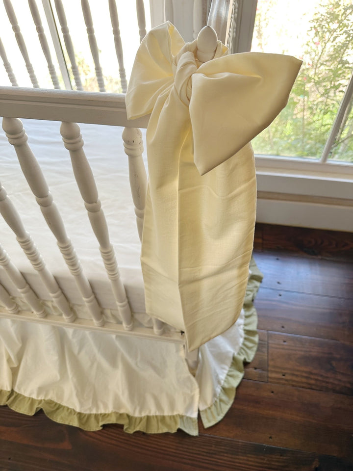 Large ivory crib bow sash hanging beside the sage green ruffle hem of the crib skirt