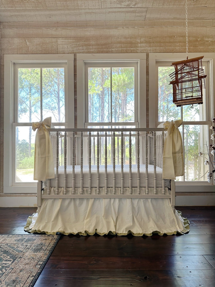 Ivory and sage crib skirt and bow set styled in a farmhouse nursery with shiplap walls and pine tree views