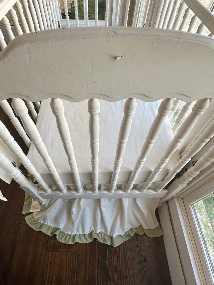 Overhead view of the ivory ruffled crib skirt with sage green trim showing full floor length coverage