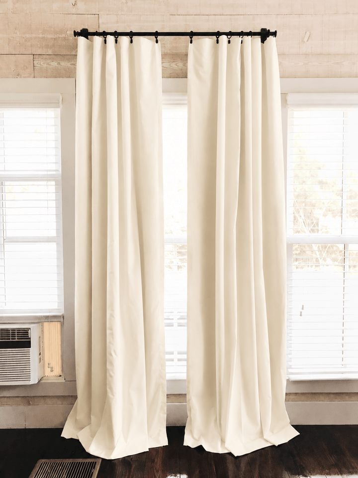 Ivory blackout curtains pulled open either side of a bright window, pooling slightly on dark floorboards