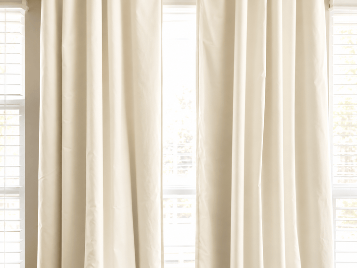 Ivory blackout panels framing a window between two white blinds on a warm grey wall