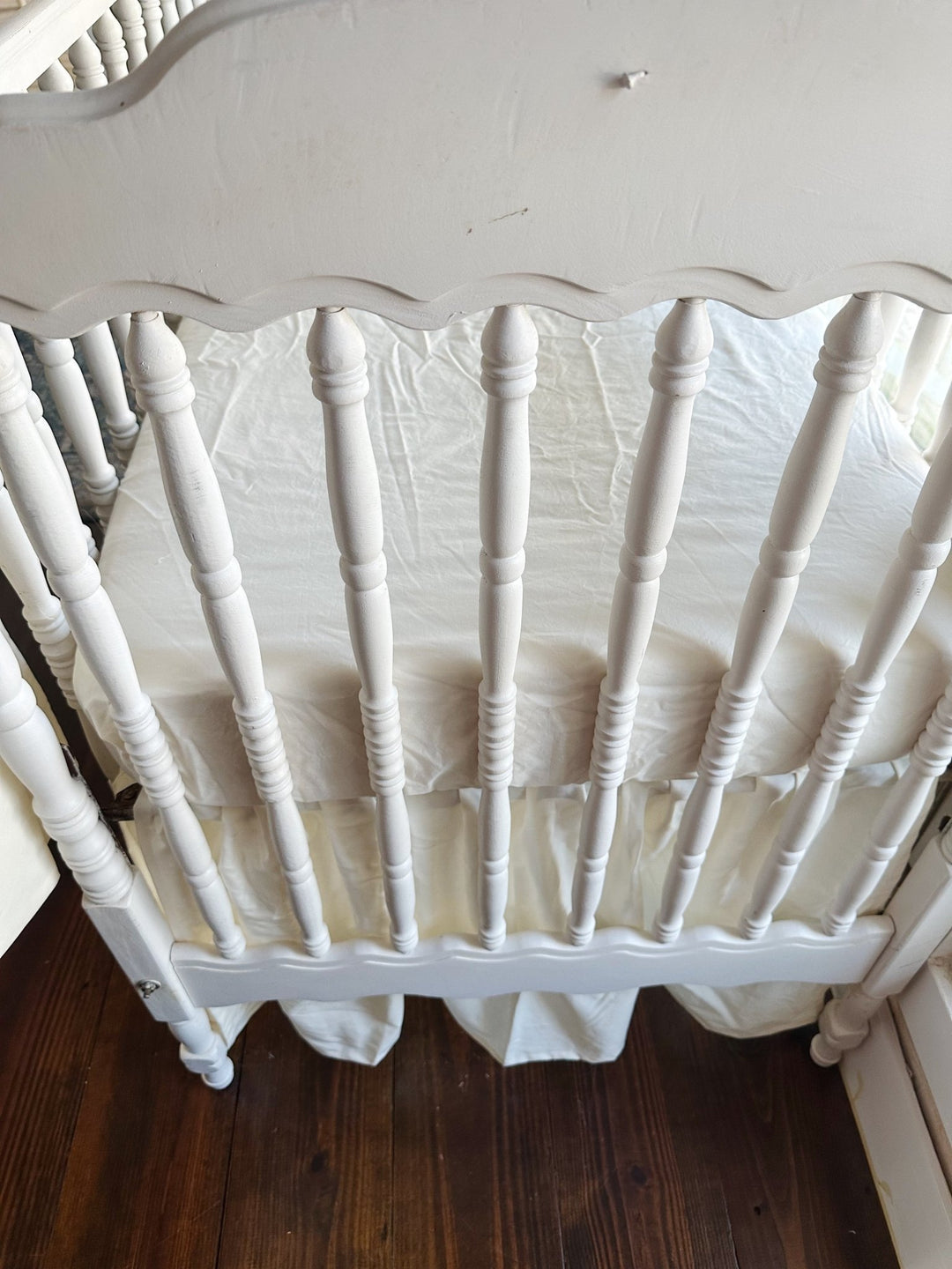 Close overhead view of the scalloped headboard spindles with the ivory skirt gathered beneath the mattress