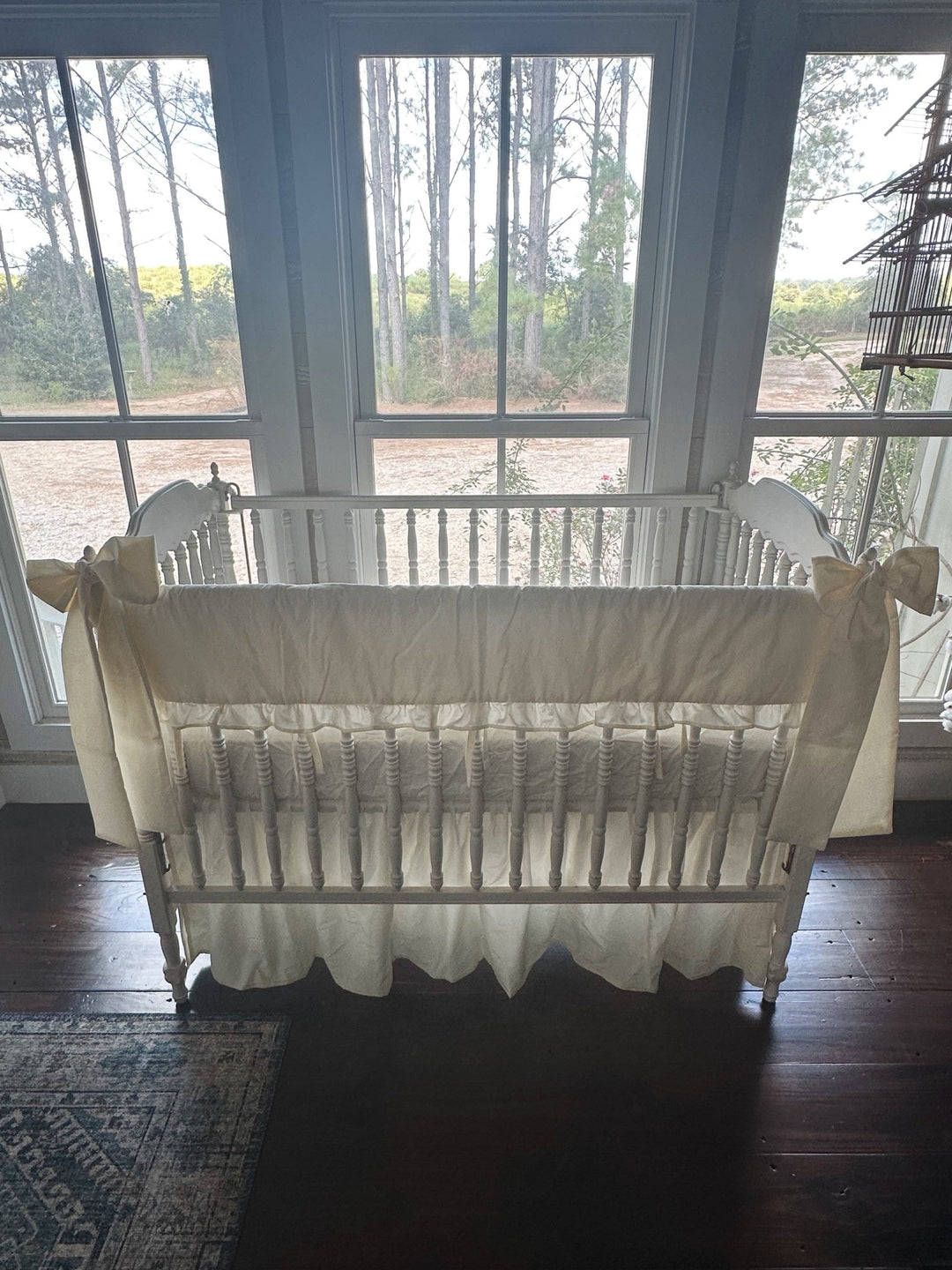 Backlit front view of the ivory ruffled rail cover set against three windows, farmhouse skirt falling to dark wood floors