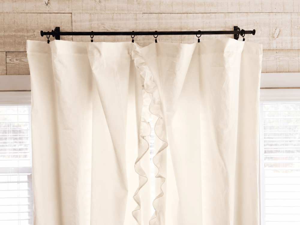 Top of the ivory ruffled curtain panels on iron rings, showing the gathered heading against shiplap - High Cotton Textile