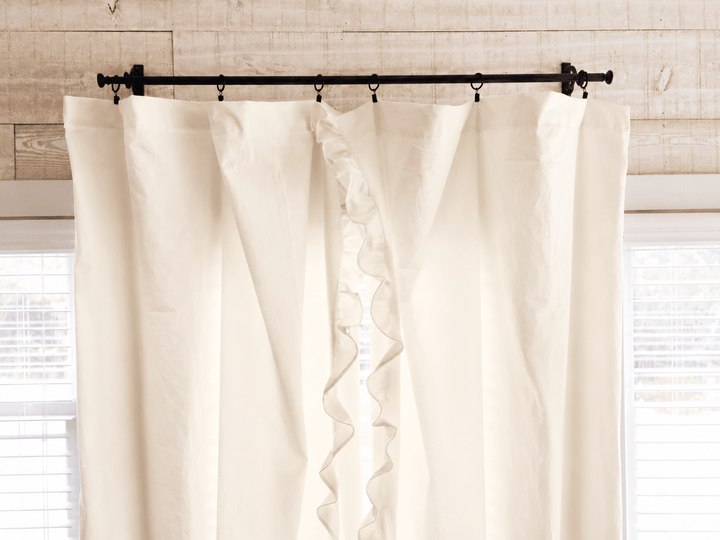 Top of the ivory ruffled curtain panels on iron rings, showing the gathered heading against shiplap - High Cotton Textile