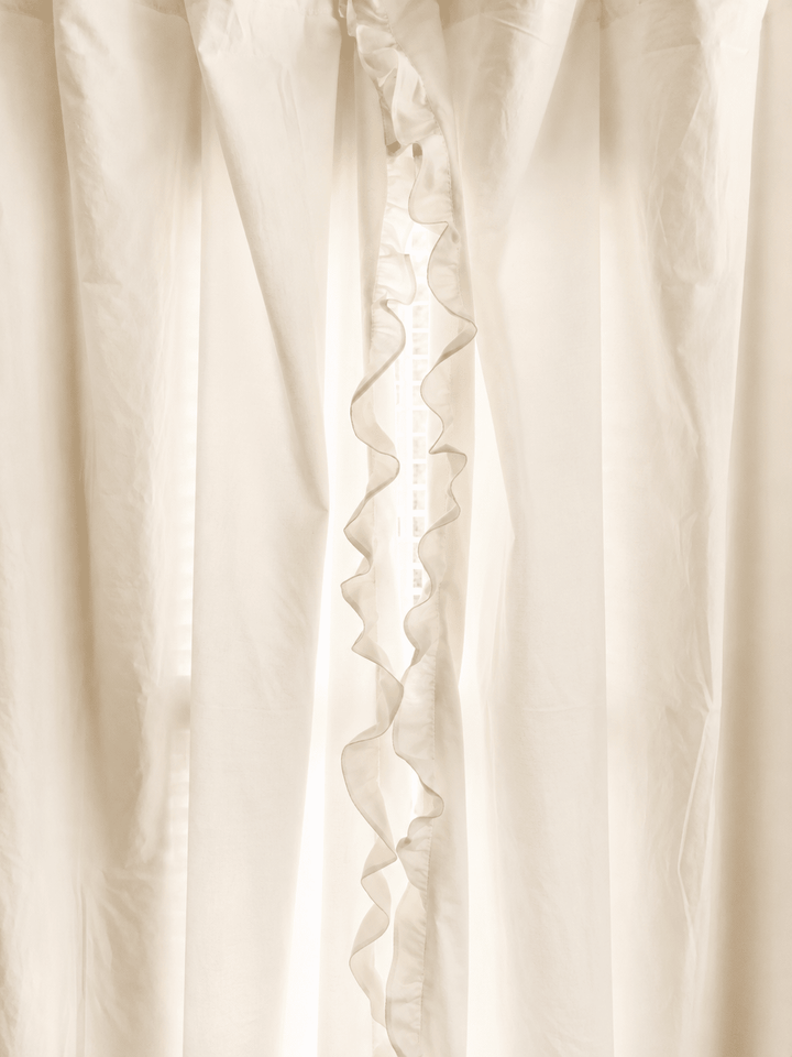 Ivory ruffled curtain panels parted at the center, the ruffle running the full length of the leading edge - High Cotton Textile