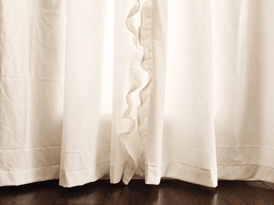 Hem of the ivory ruffled nursery curtains where the panels meet the dark wood floor - High Cotton Textile