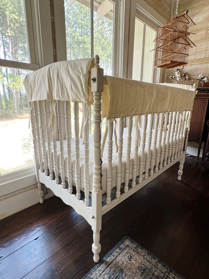 Angled view of ivory rail covers on both the long side and end rails of a spindle crib