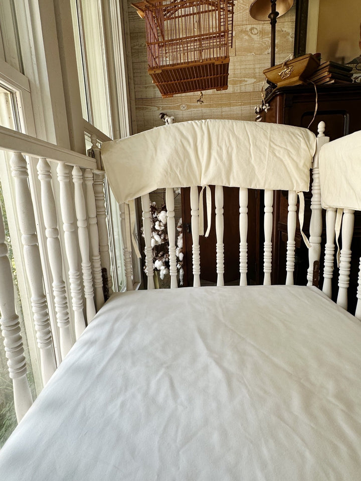 Ivory rail cover on the crib rail with cotton stems and a vintage birdcage in the background