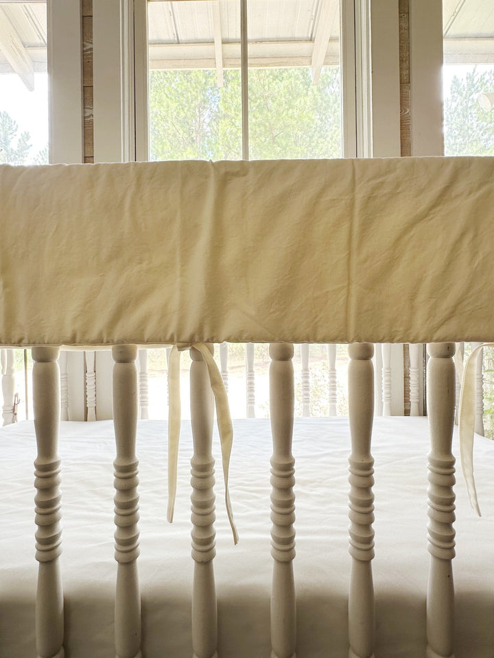 Close view of the ivory cover draped over the crib top rail with ties hanging between spindles