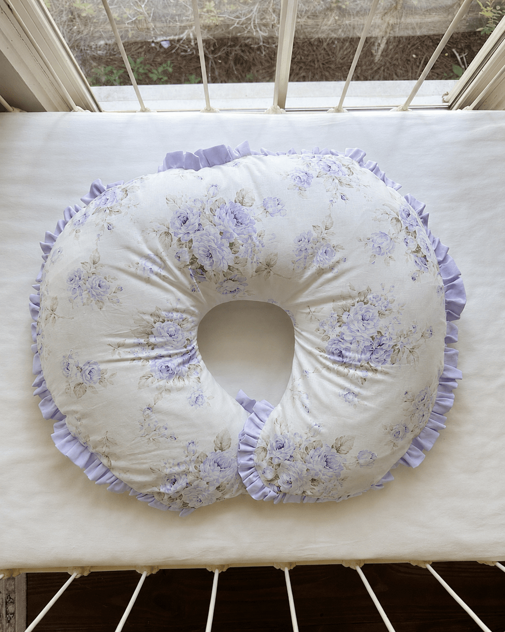 Lavender floral ruffled nursing pillow cover styled on a crib mattress in a lavender baby girl nursery