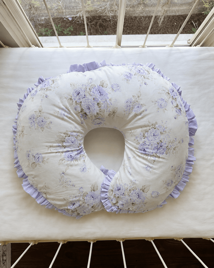 Lavender floral ruffled nursing pillow cover styled on a crib mattress in a lavender baby girl nursery