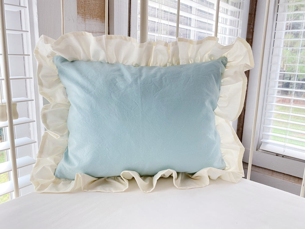 Mist and ivory ruffled crib pillow propped against the rail of an antique iron crib