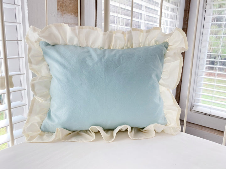 Mist and ivory ruffled crib pillow propped against the rail of an antique iron crib