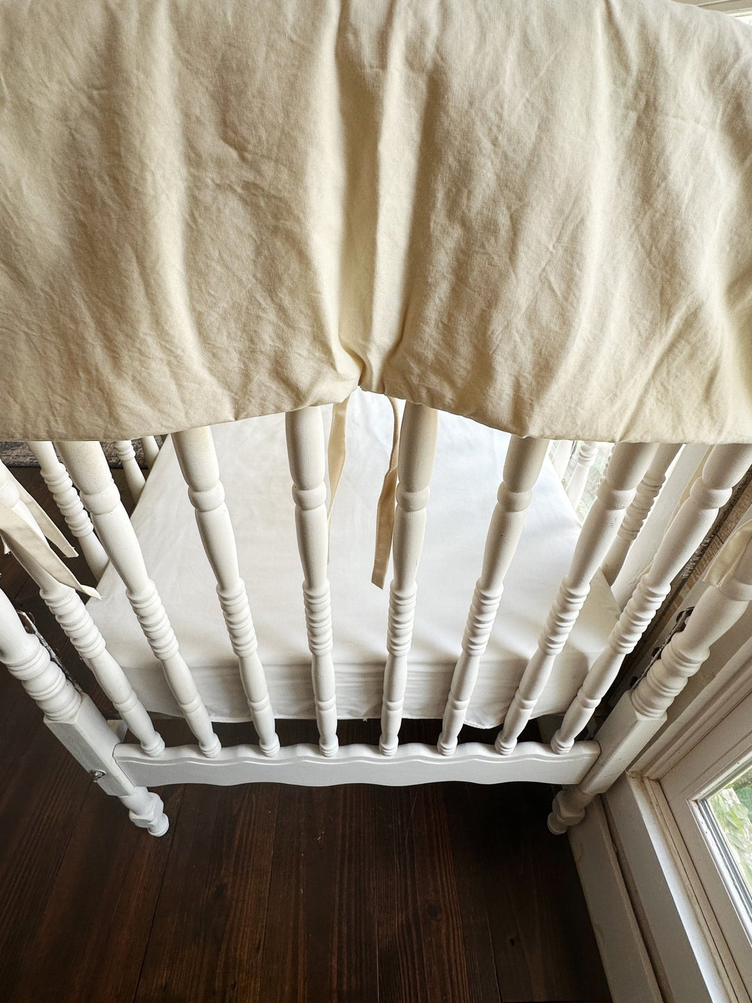 Natural crib rail cover draped over the corner top rail of a white spindle crib with soft cotton ties