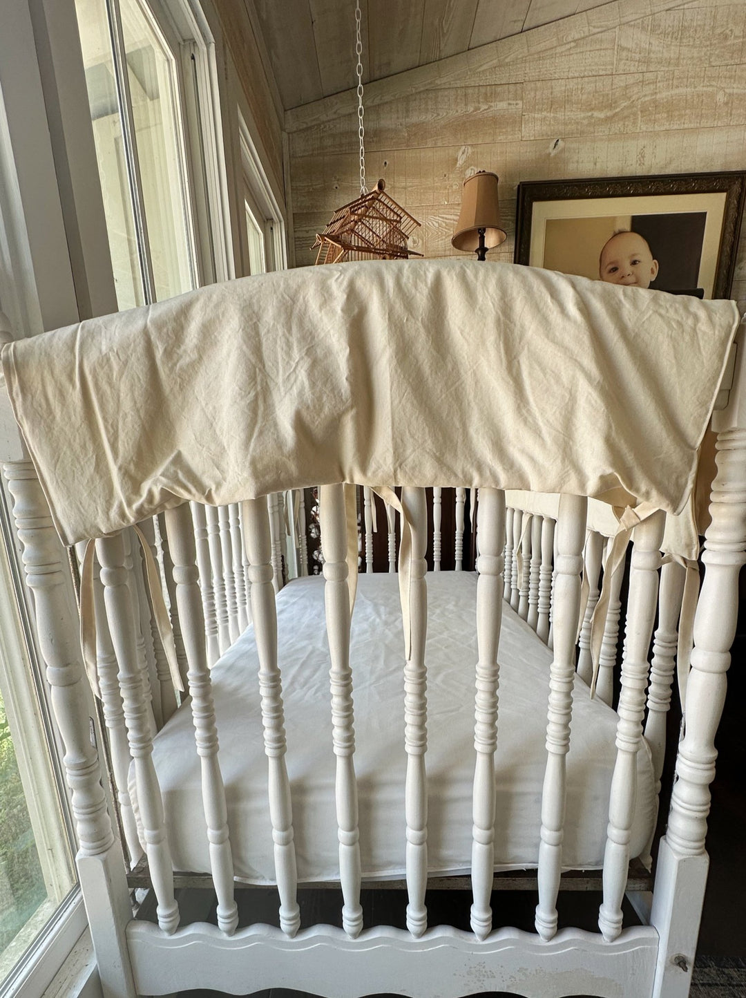 Short end Natural crib rail cover in neutral beige tied onto a white spindle crib