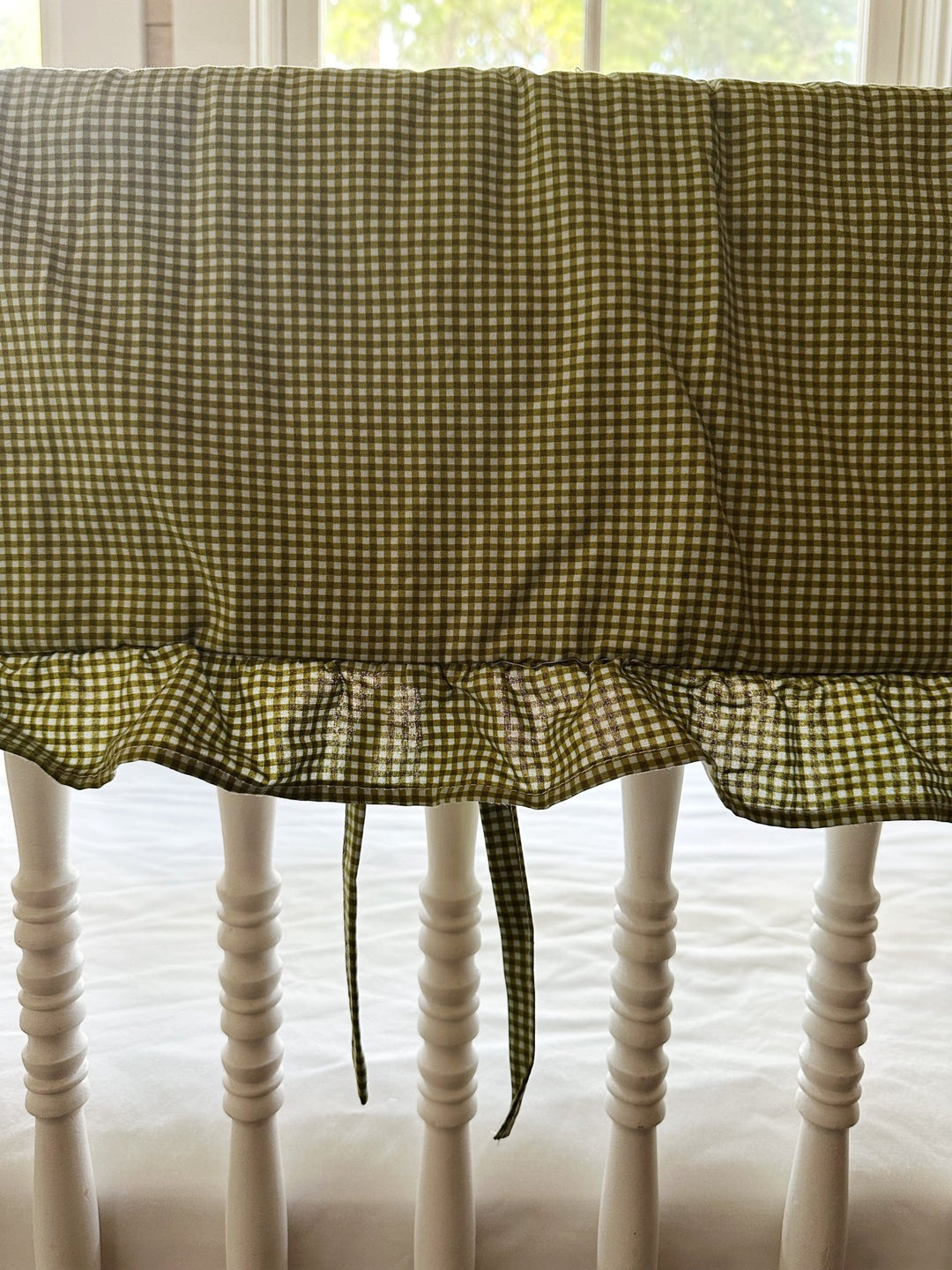 Ruffle edge and tiny fabric ties on the green gingham crib rail cover, backlit by a window