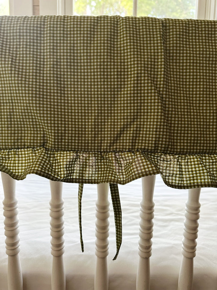 Ruffle edge and tiny fabric ties on the green gingham crib rail cover, backlit by a window