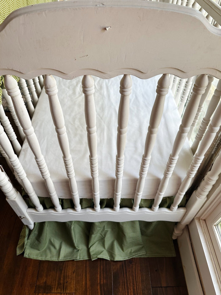 White spindle crib end with green gingham crib skirt and a white crib sheet