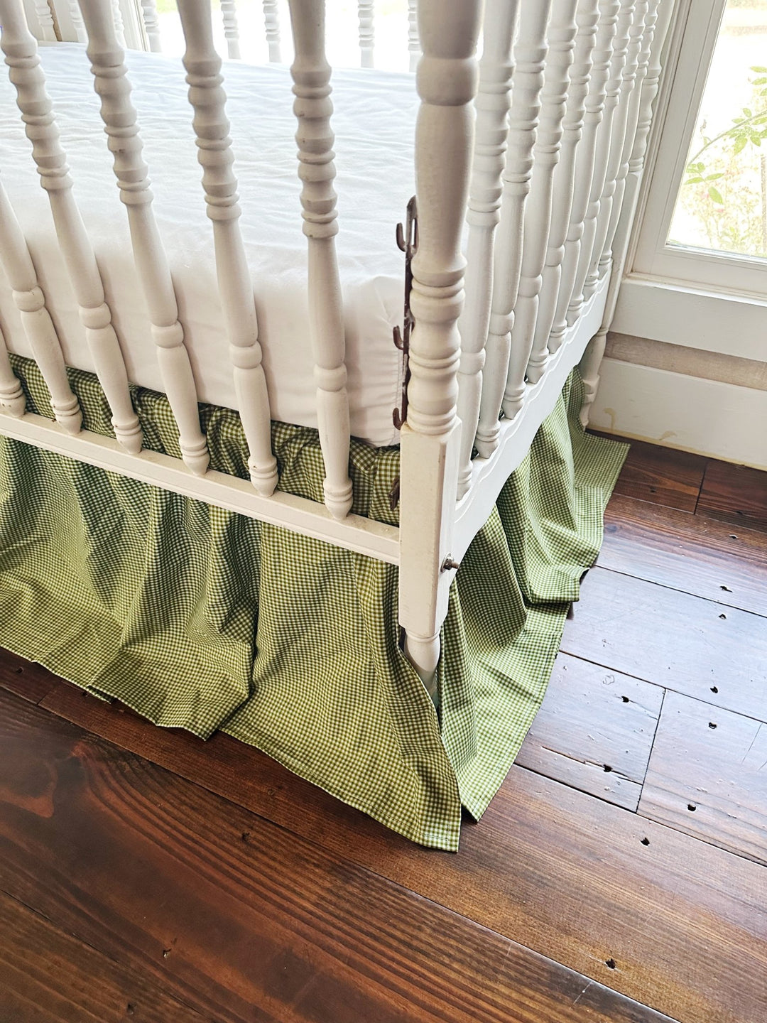 Corner view of the 20 inch pine green gingham crib skirt reaching toward a wood floor