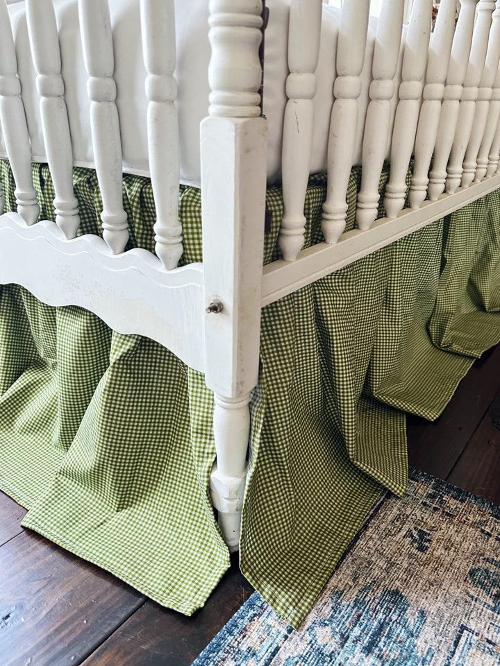 Split corner detail of the pine green gingham crib skirt wrapping around a white crib leg