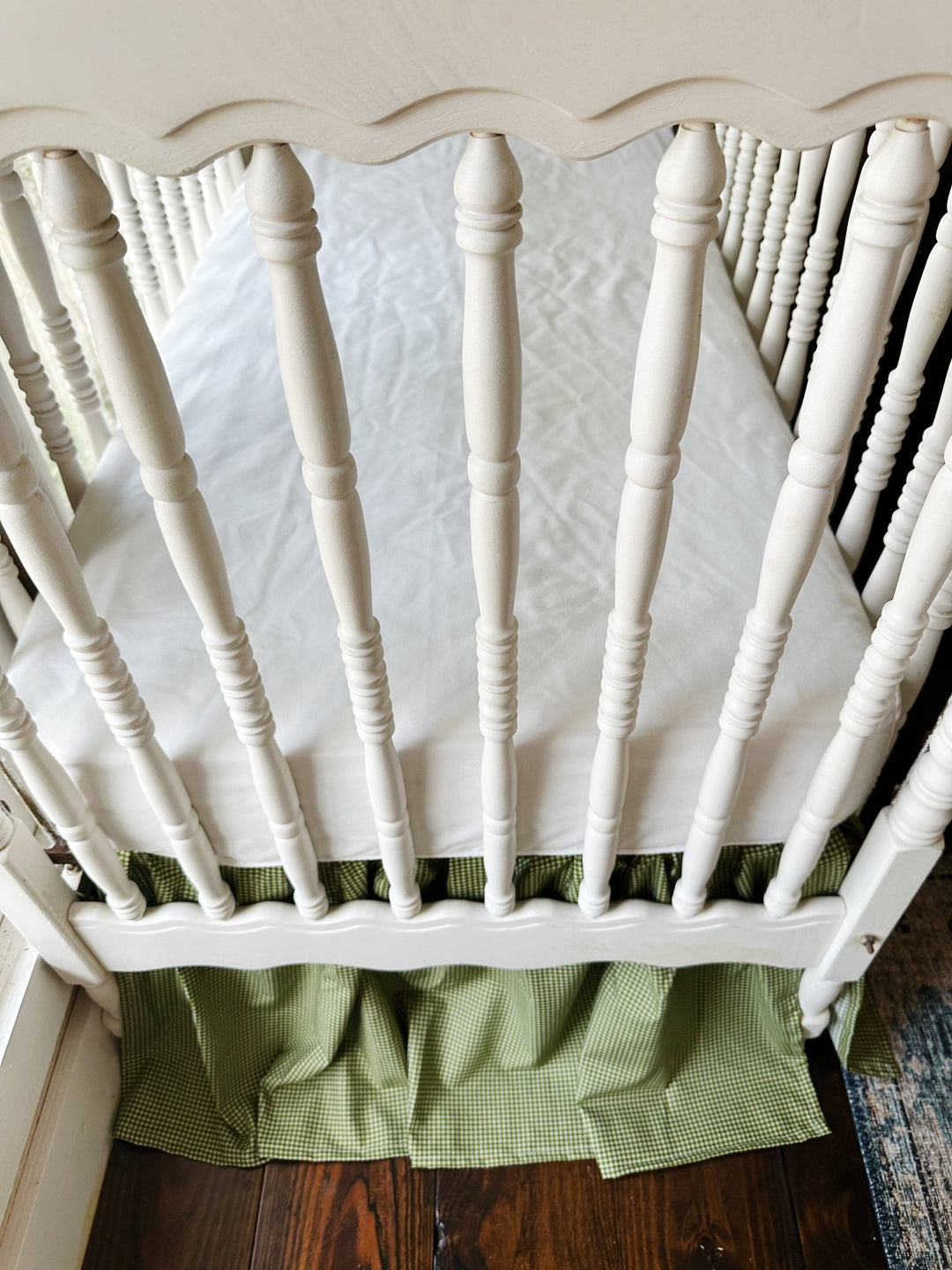 Overhead view of a white spindle crib with the green gingham farmhouse crib skirt